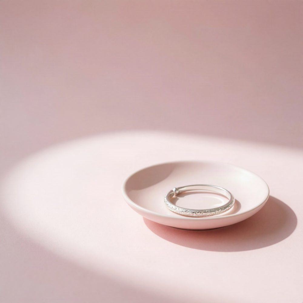 Pulseira prateada ornamentada em prato rosa claro com sombra suave sobre fundo rosa