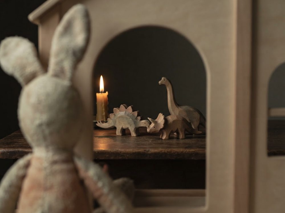 Coelho de peluche olhando brinquedos de dinossauros de madeira junto a uma vela acesa