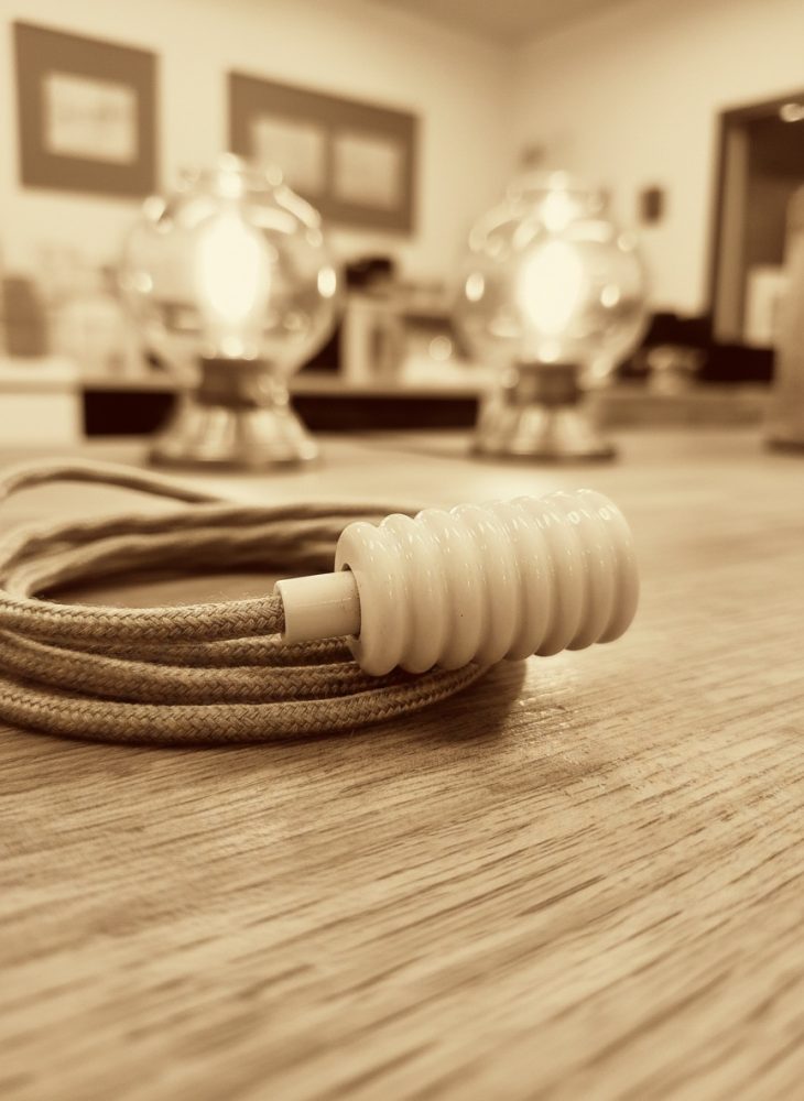Interruptor de fio têxtil branco sobre mesa de madeira com luzes suaves ao fundo