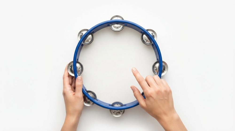 Mãos a segurar e tocar uma castanhola azul com címbalos metálicos sobre fundo branco