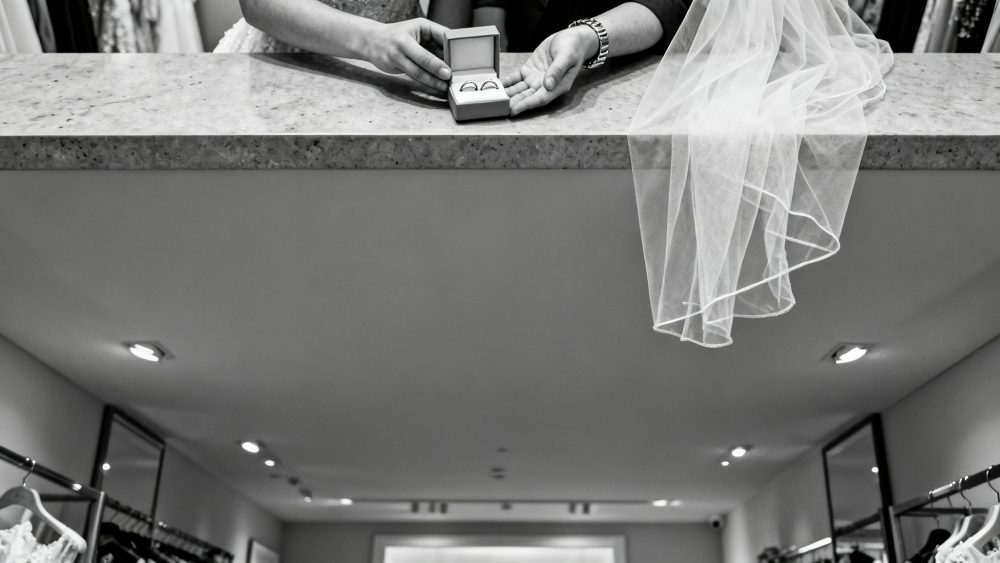 Caixa aberta com alianças de casamento sobre balcão com véu branco e mãos a segurá-la em loja