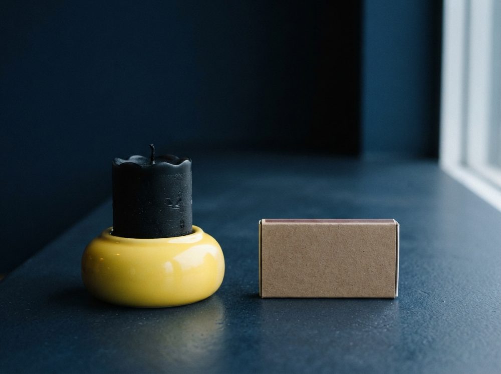 Vela preta num suporte amarelo com caixa castanha de fósforos ao lado, sobre mesa escura