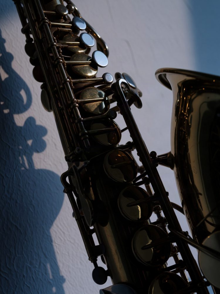 Saxofone preto com teclas metálicas refletindo luz e sombra projetada na parede branca azulada