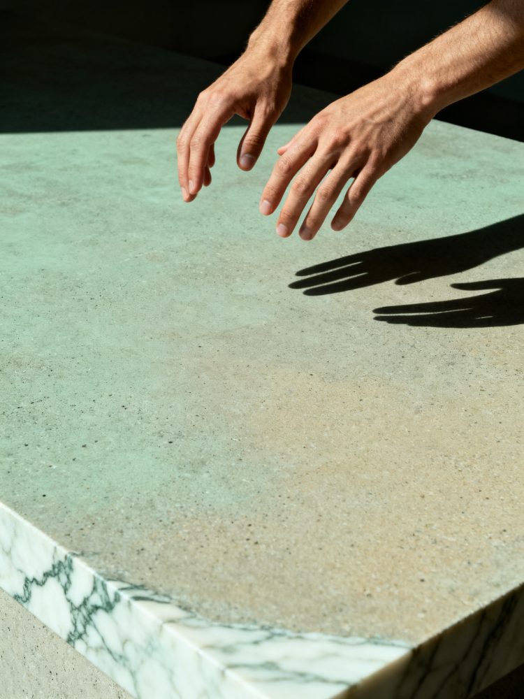 Mãos pairando sobre superfície de betão cinzento com borda de mármore branco e sombras
