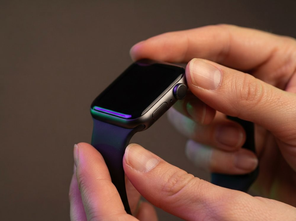 Mãos segurando relógio inteligente com ecrã desligado e pulseira preta