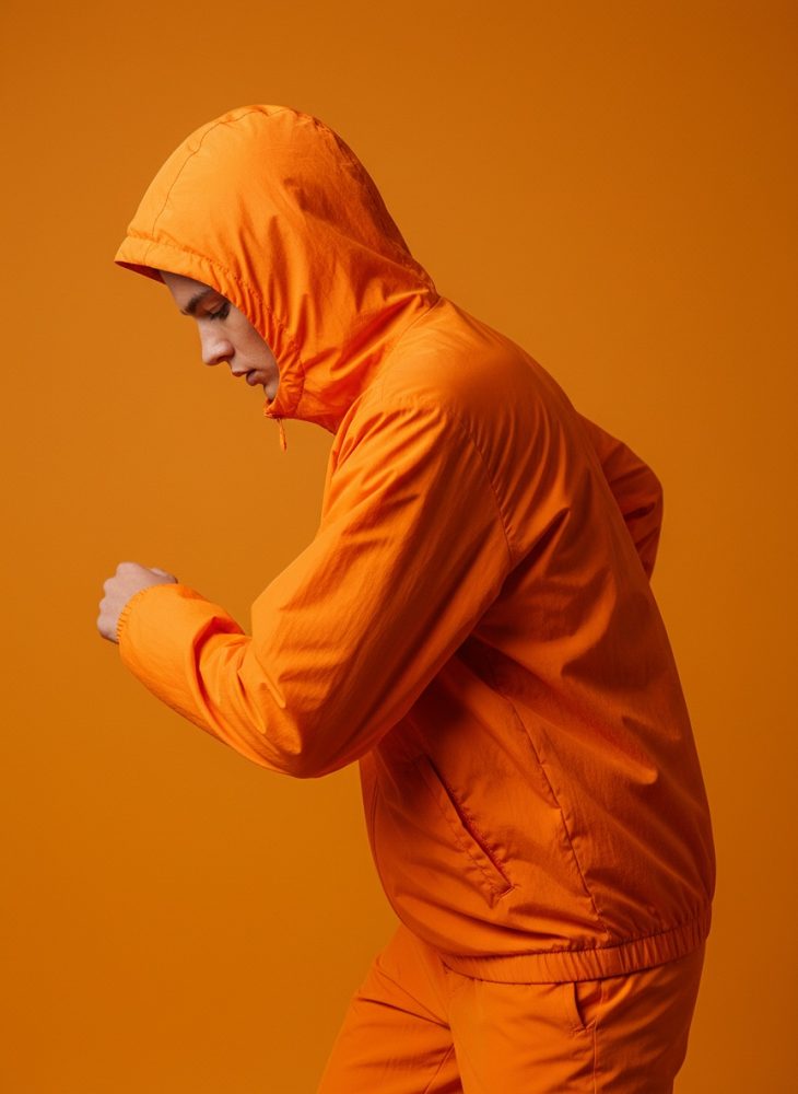 Pessoa de perfil com casaco e capuz laranja em fundo laranja monocromático