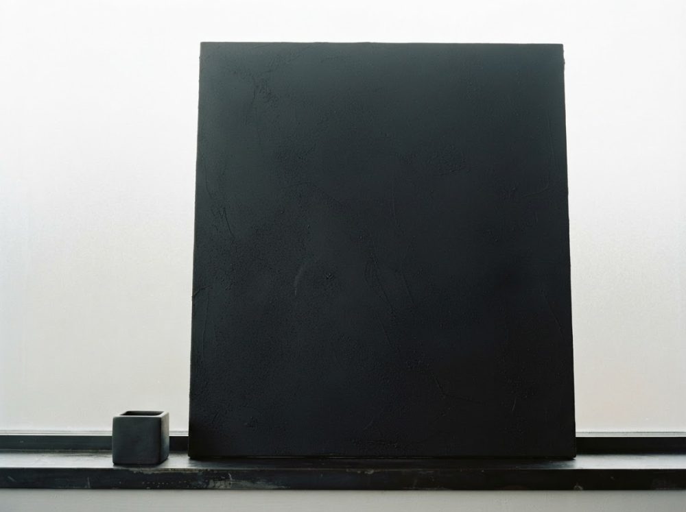 Painel preto quadrado e vaso pequeno preto sobre prateleira com fundo branco