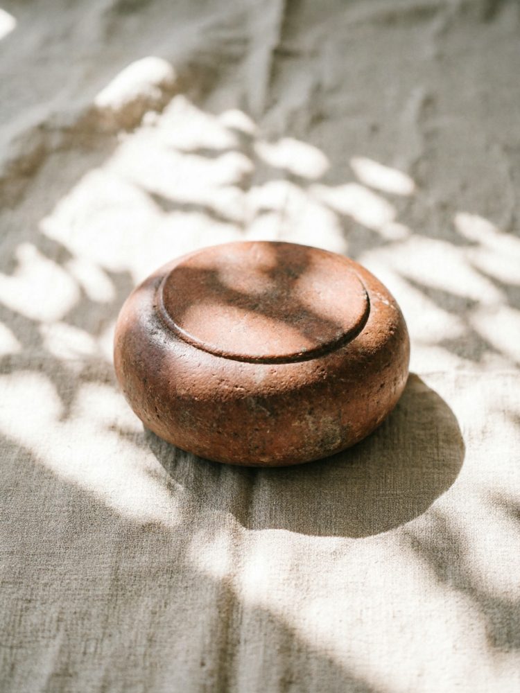 Pedra de peso circular castanha sobre tecido claro com sombras naturais