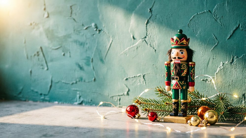Boneco Quebra-Nozes decorativo prata entre ramos de pinheiro e bolas natalícias coloridas com luzes