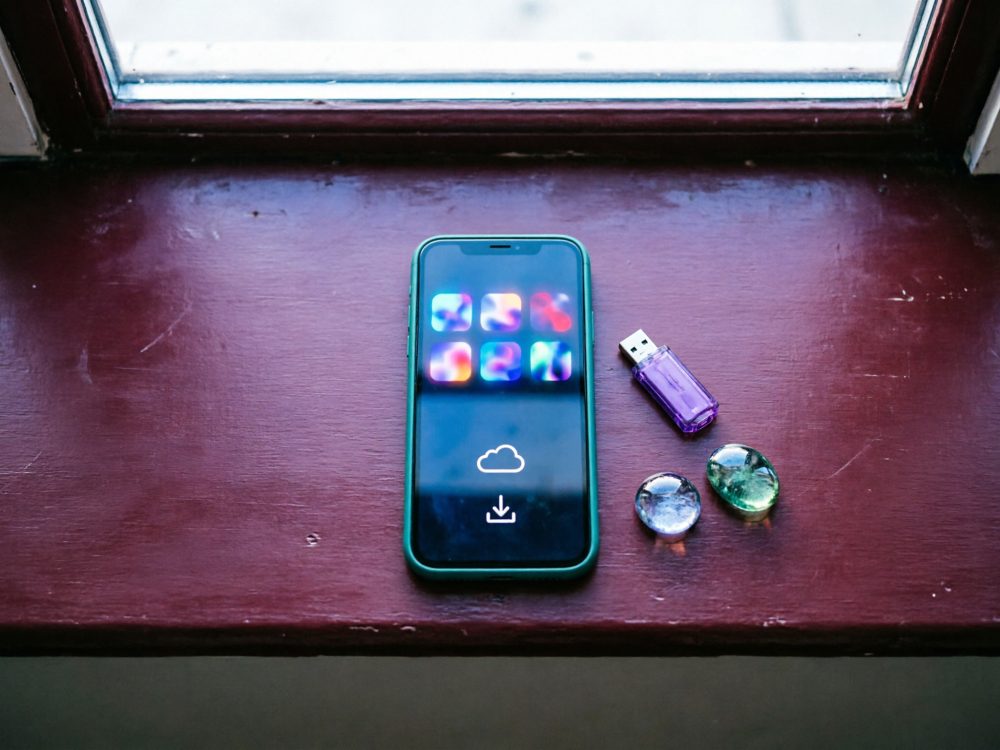 Smartphone com ecrã de apps digitais e pen USB roxa numa superfície de madeira castanha junto a dois objetos transparentes
