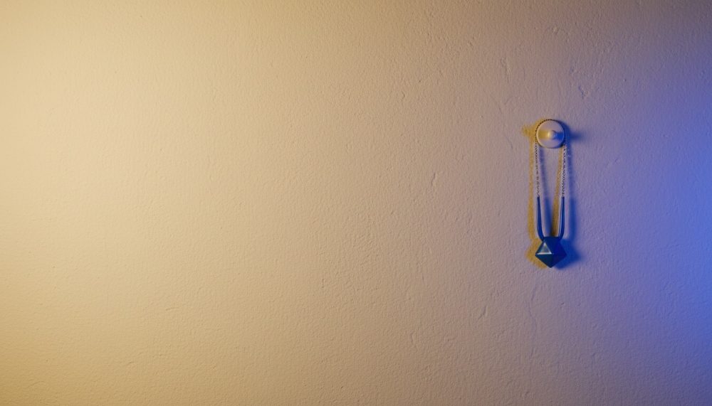 Colar pendurado em botão branco numa parede iluminada por luz amarela e azul
