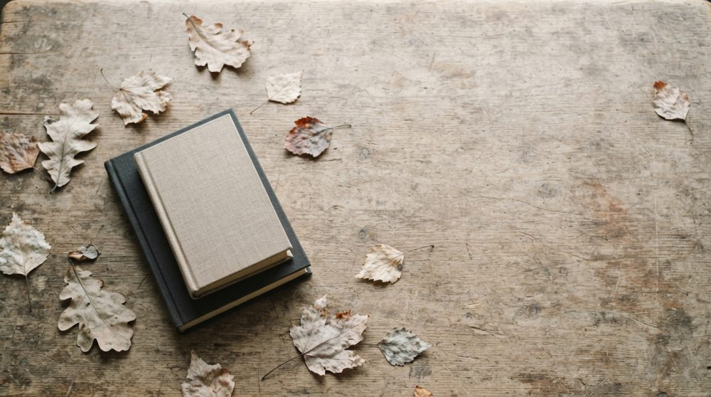 Dois livros com capas neutras sobre mesa de madeira envelhecida rodeados por folhas secas