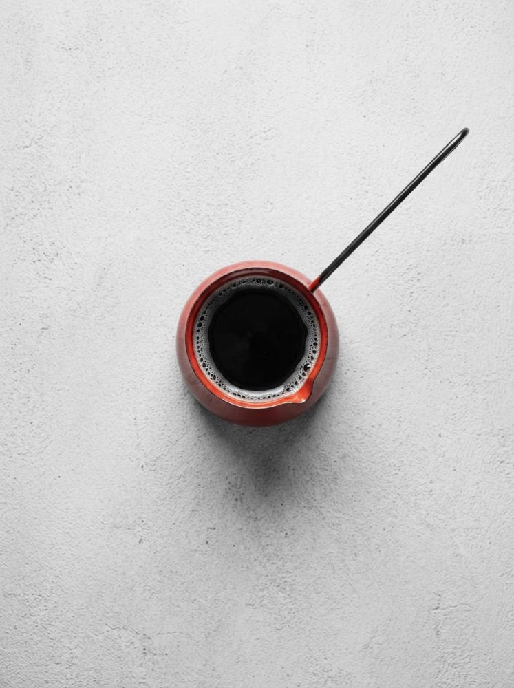 Cafeteira turca vermelha com café preto, vista de cima sobre fundo branco texturado