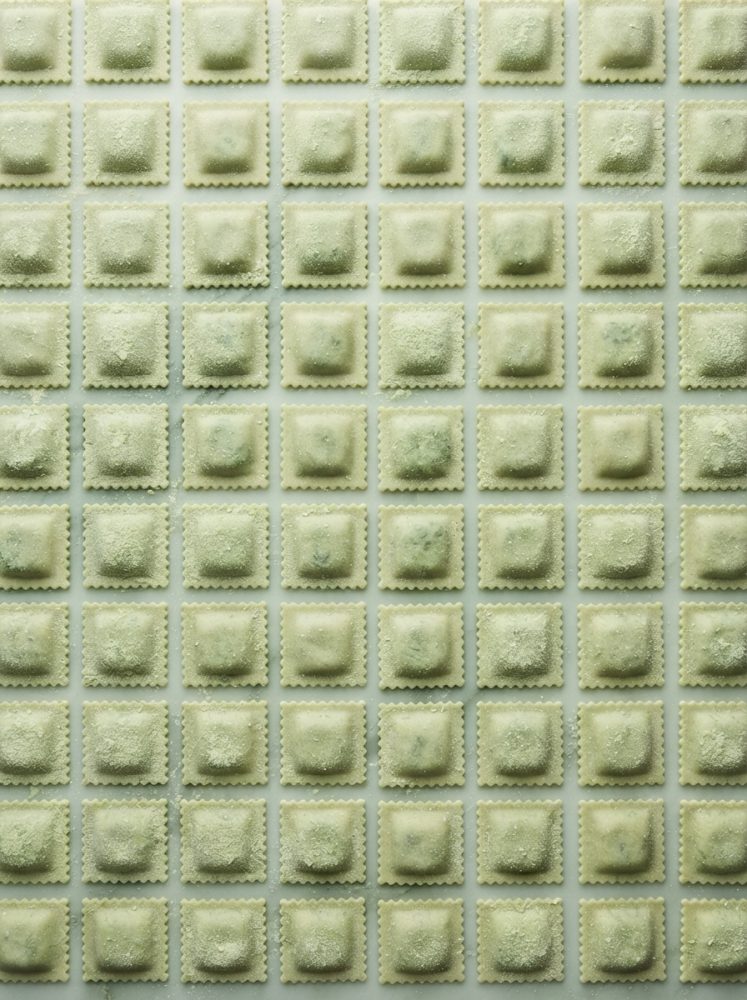 Raviolis frescos quadrados dispostos em padrão uniforme sobre superfície branca