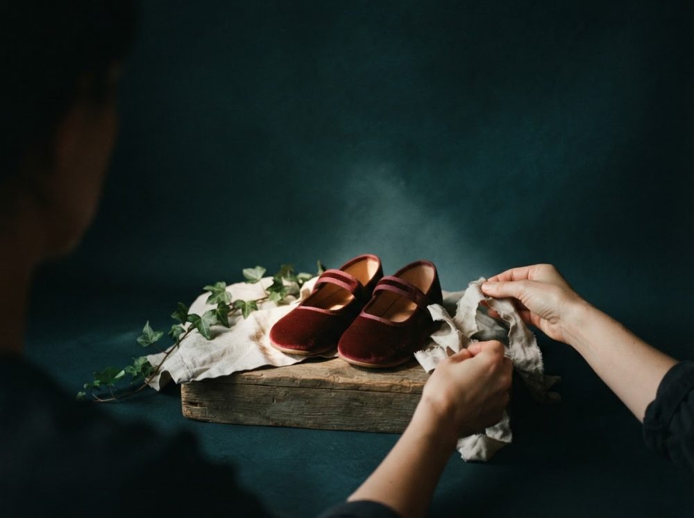 Par de sapatos infantis bordô de veludo em caixa de madeira com folhas verdes e pano branco