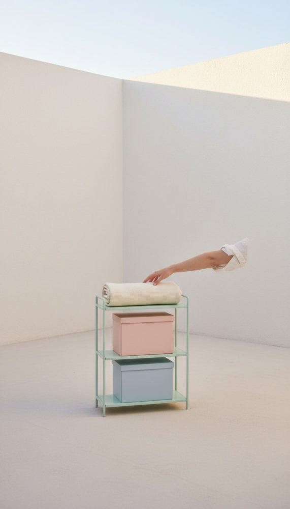 Estante verde com caixas rosa e azul e manta branca dobrada, fundo claro minimalista