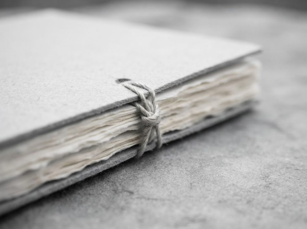 Caderno artesanal com capas cinzentas e folhas rústicas unido por fio trançado