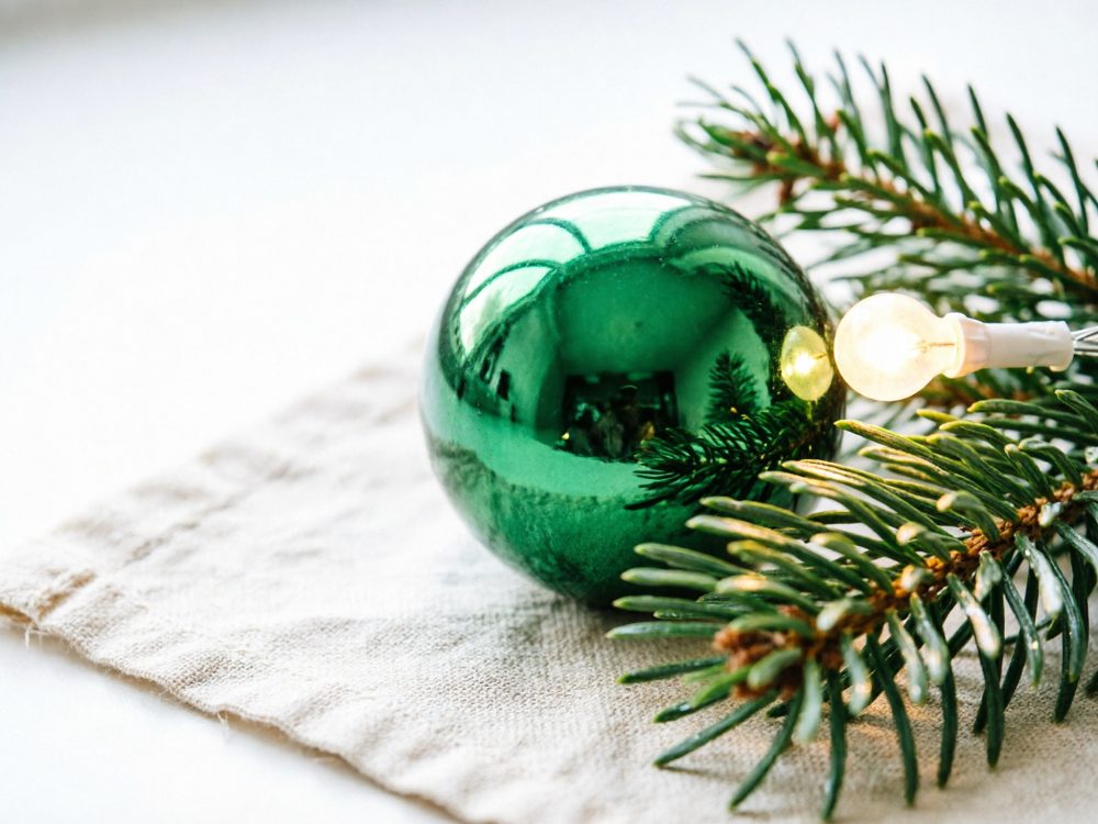 Bola verde de Natal com raminho de pinheiro e luz amarela sobre tecido branco