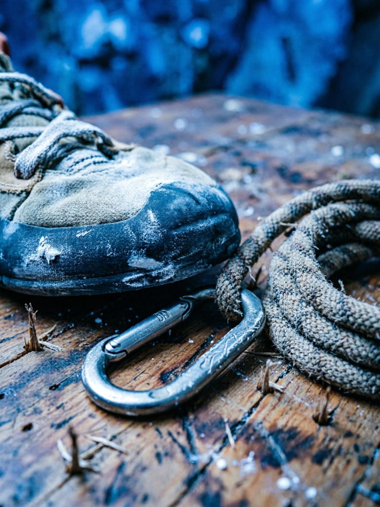 Bota de escalada usada, mosquetão metálico e corda sobre madeira rústica