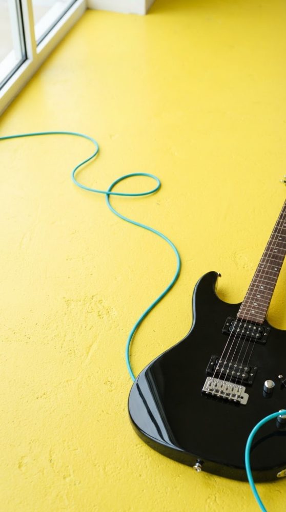 Guitarra elétrica preta com cabo azul com fundo amarelo vibrante e texturizado