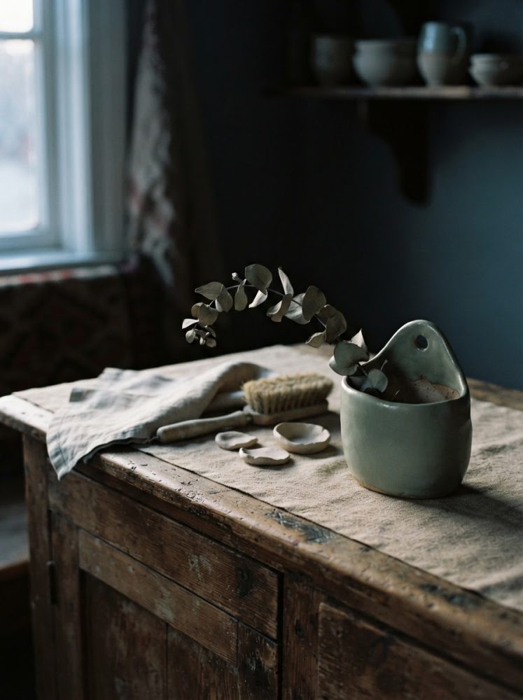 Utensílios artesanais e vaso de cerâmica com ramo seco sobre mesa rústica de madeira