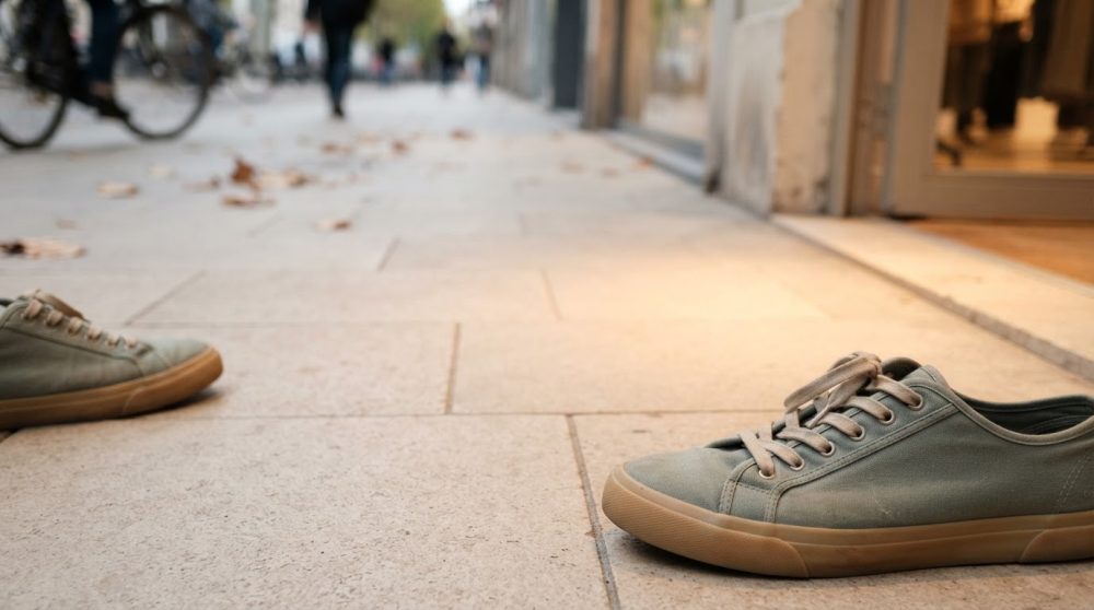 Ténis verdes com sola castanha colocados no chão calcetado numa rua com ambiente citadino