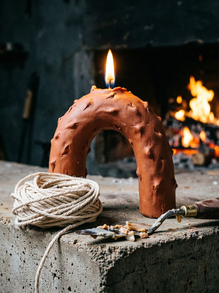 Vela castanha em forma de arco junto a corda enrolada, com fogo aceso ao fundo