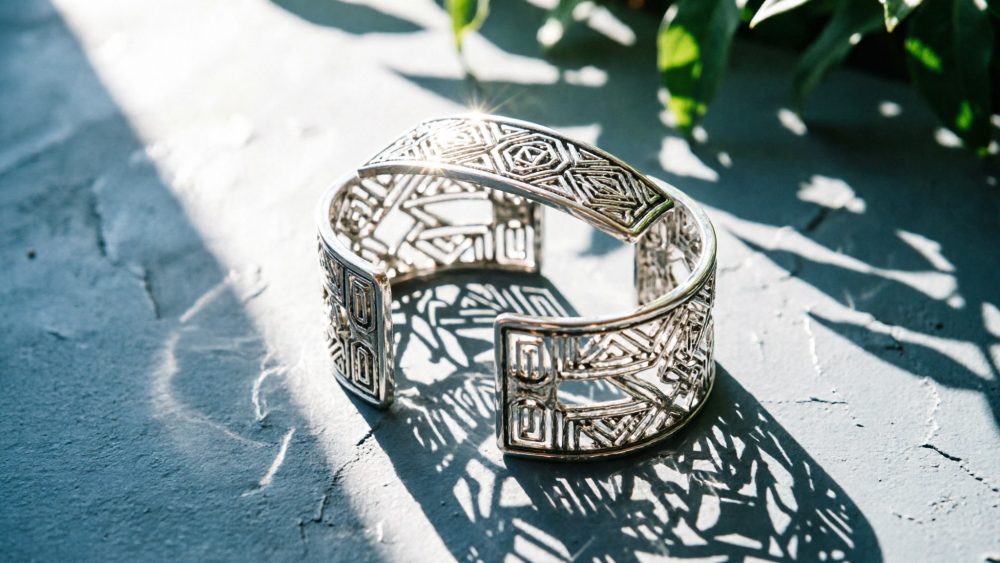 Pulseira de prata aberta com padrão geométrico em luz natural e sombras