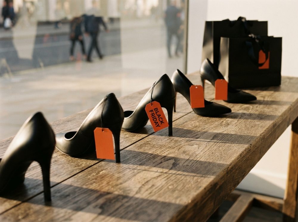 Linha de sapatos de salto alto pretos com etiquetas vermelhas de Black Friday numa mesa de madeira