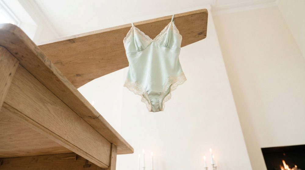 Body azul claro de cetim com rendas creme pendurado em estrutura de madeira clara