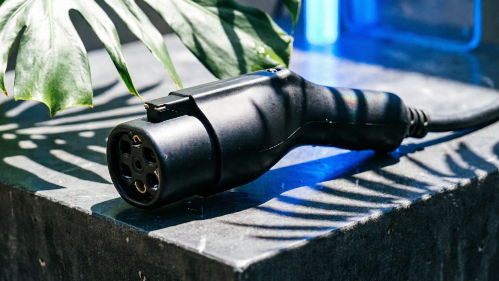 Cabo de carregamento preto de automóvel elétrico numa superfície cinzenta com sombras de folhas