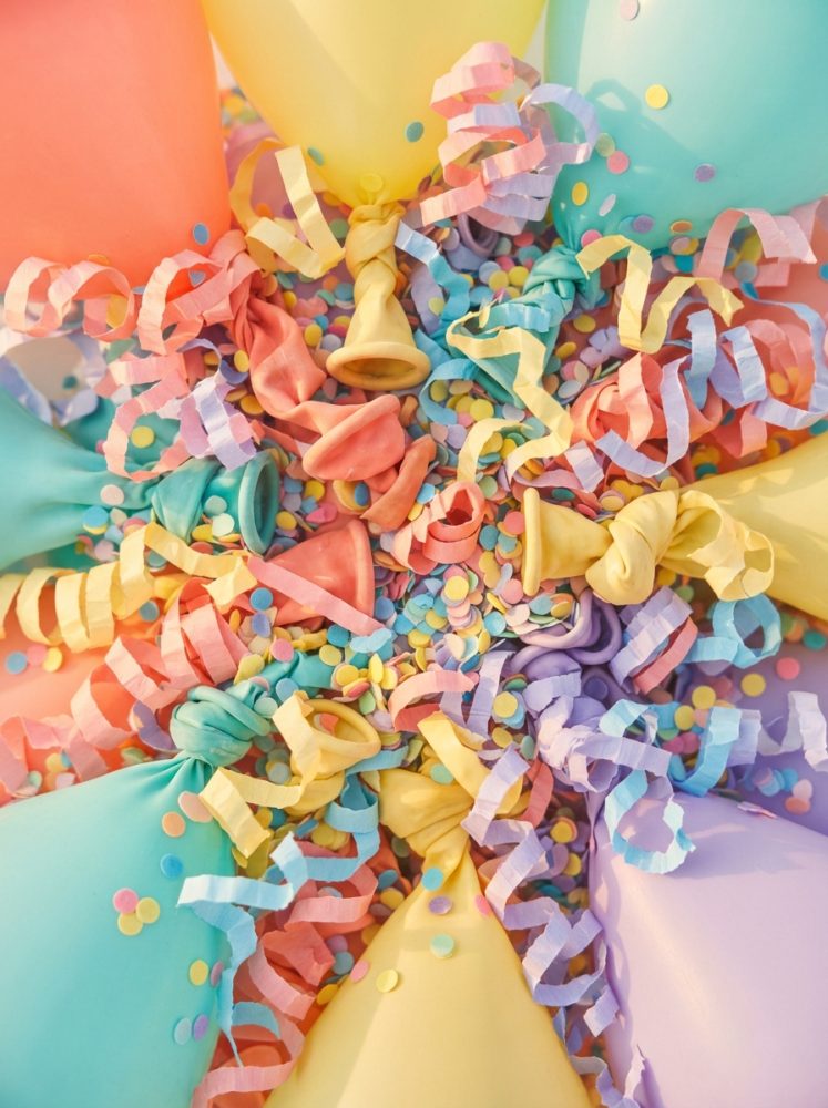 Balões coloridos com serpentinas e confetes espalhados em fundo claro para festa
