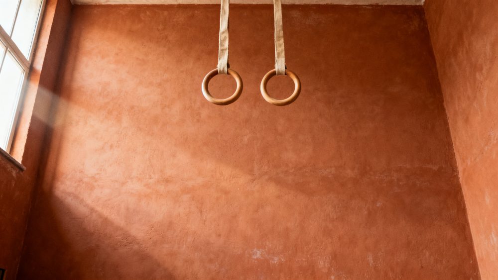 Argolas de ginástica de madeira penduradas em teto contra parede terracota iluminada