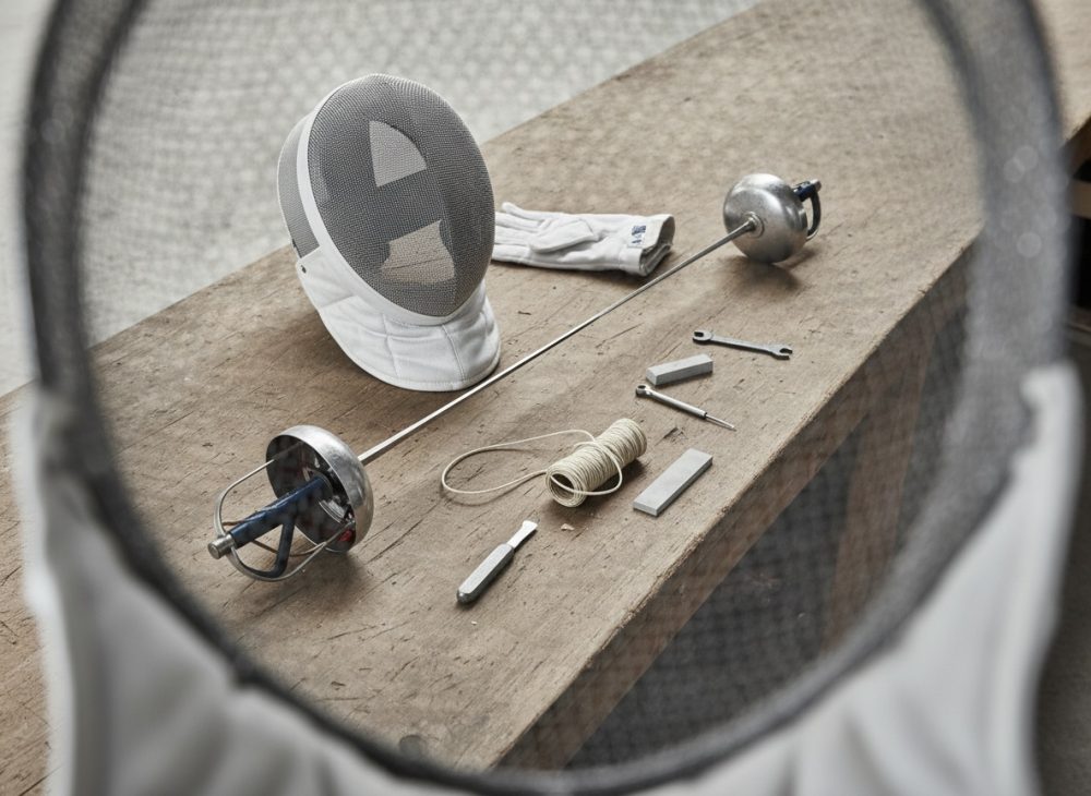 Conjunto de equipamentos de esgrima com máscara, luva, florete e acessórios sobre mesa de madeira