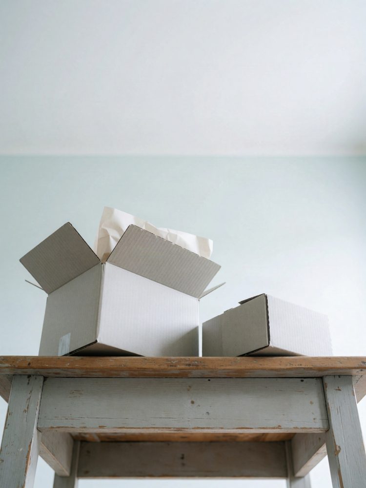 Caixas de cartão branco, uma aberta com papel de embalagem, sobre mesa de madeira rústica