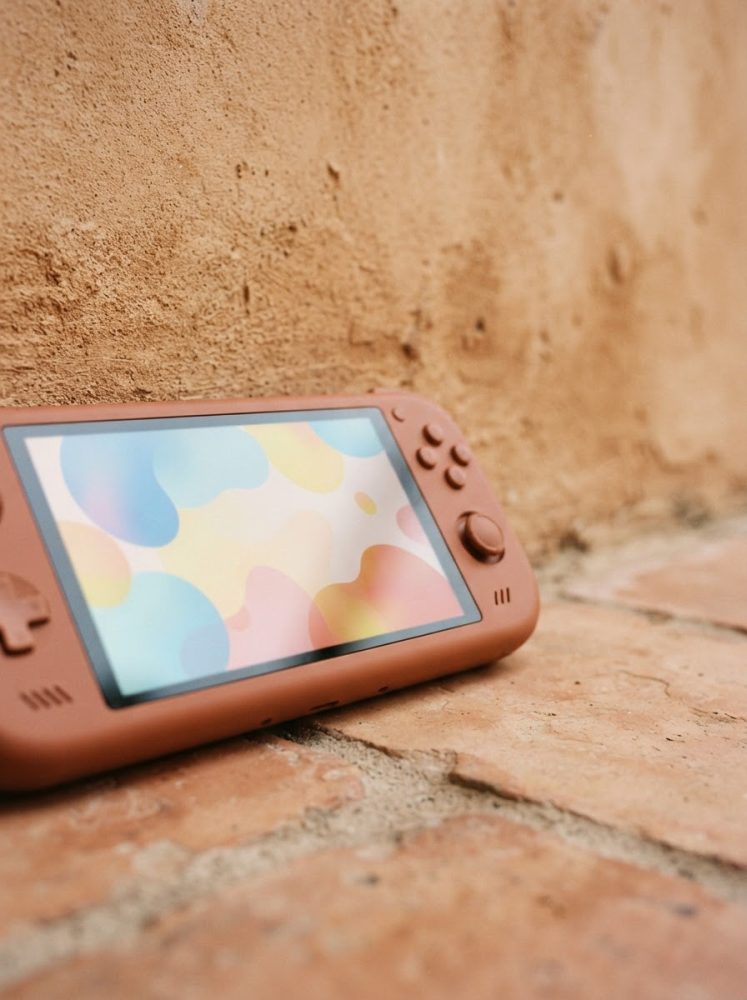 Consola portátil castanha de videojogos sobre chão e parede de tijolos