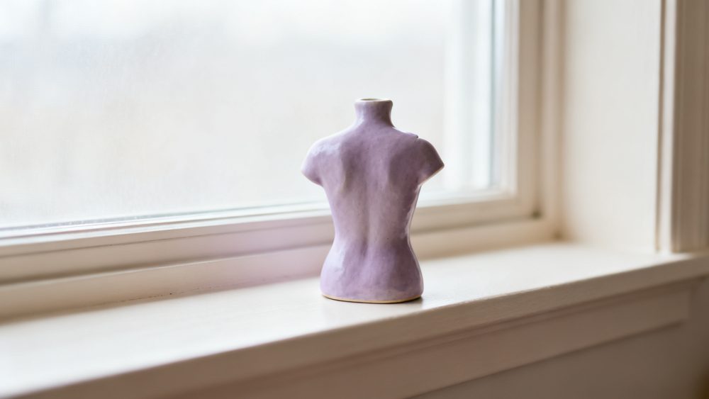 Escultura lilás cerâmica de busto feminino exposta numa janela clara e moderna