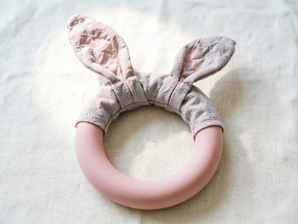 Chocalho para bebé com orelhas de coelho em tecido cinza e aro rosa claro sobre tecido claro
