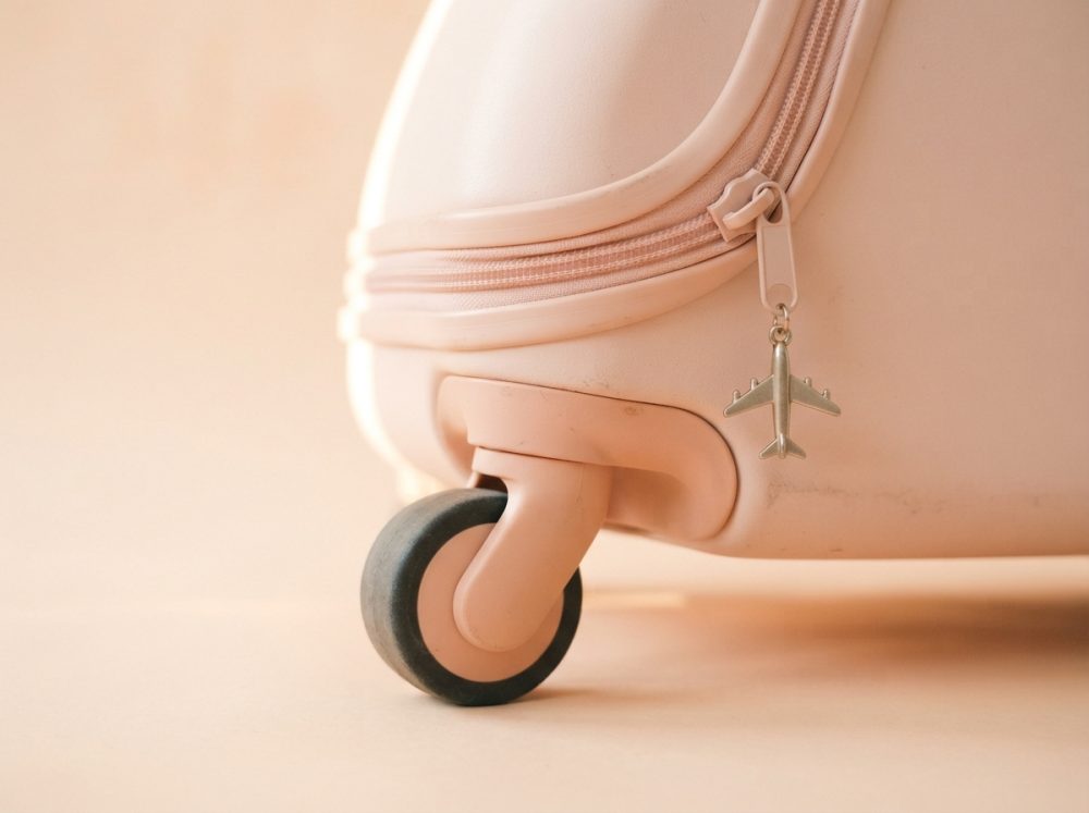 Roda da mala de viagem rosa com pendente de avião metálico