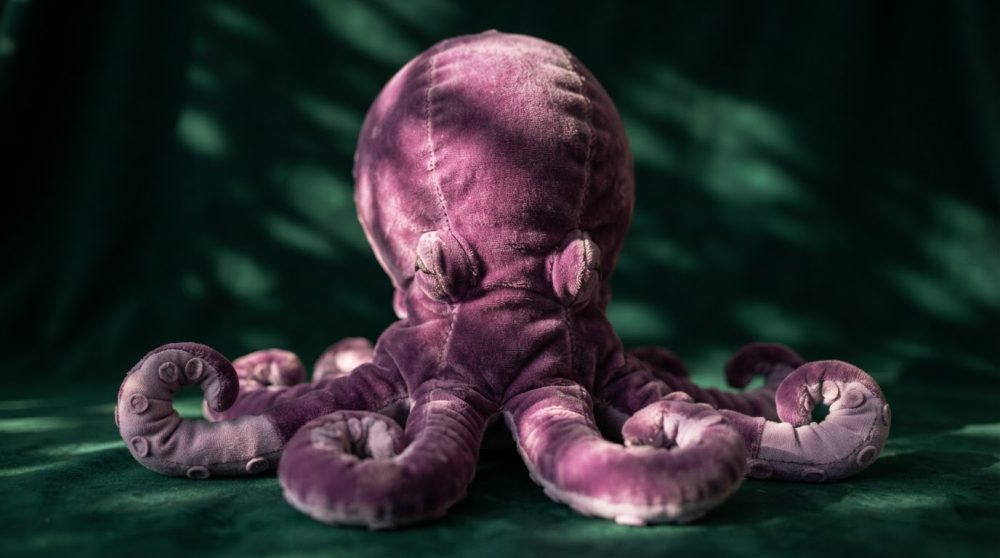 Polvo de peluche roxo com tentáculos enrolados sobre fundo escuro