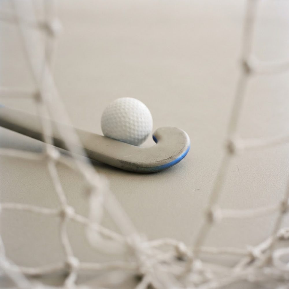 Stick de hóquei junto a bola branca com rede desfocada em fundo claro