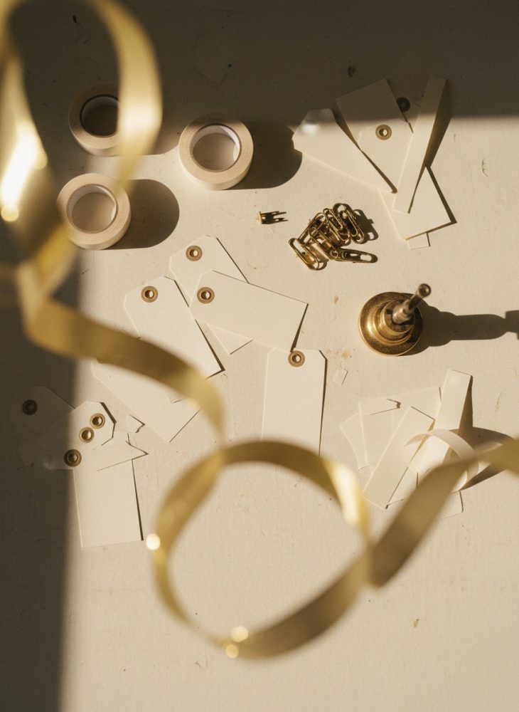 Etiquetas brancas com ilhós dourado, fita adesiva, clipes metálicos dourados e suporte metálico em mesa clara