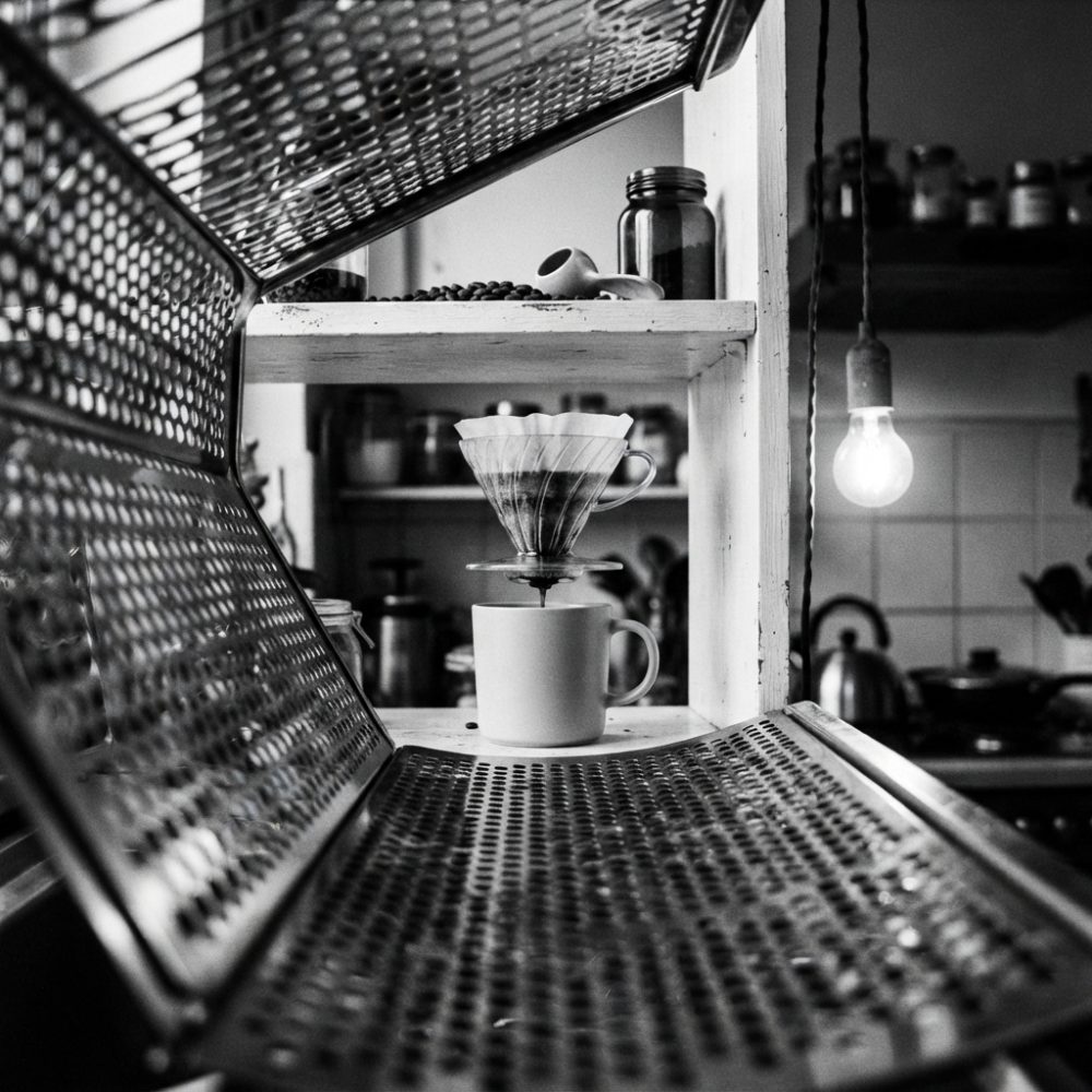 Filtro de café a escorrer para uma chávena branca numa cozinha com luz quente