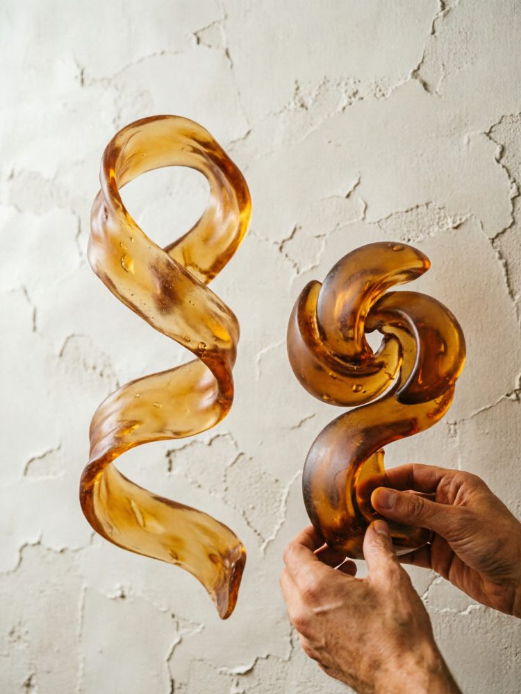 Esculturas abstratas em vidro âmbar com formas onduladas em fundo texturado