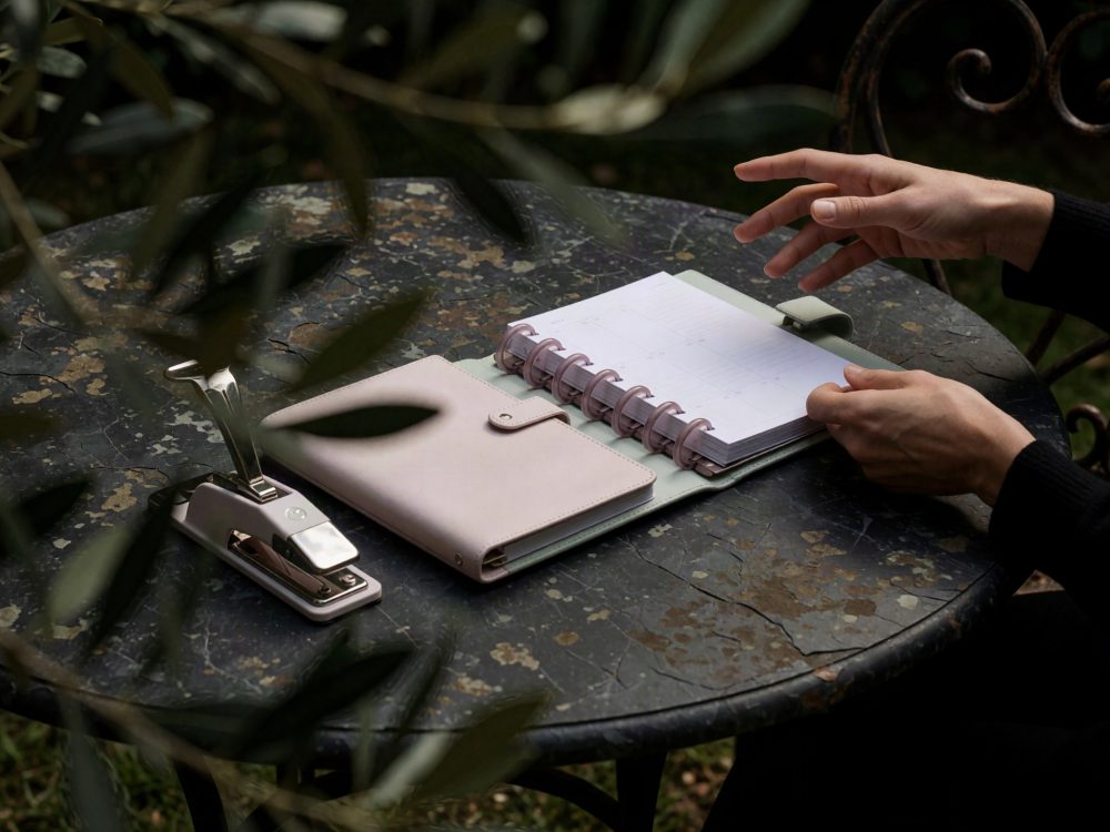 Livro de notas aberto com agenda e um grampeador sobre mesa metálica envelhecida com mãos a manusear