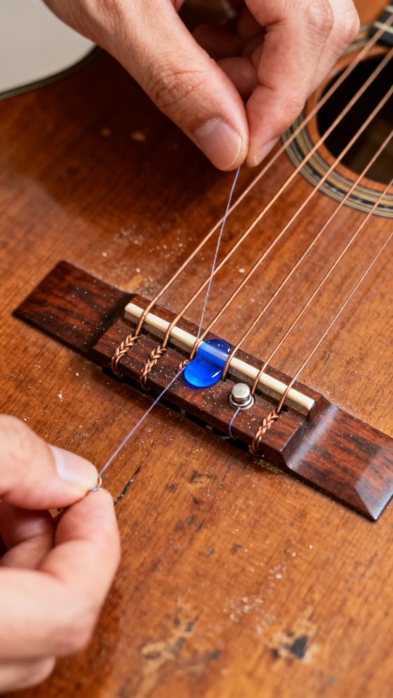 Mãos a trocar uma corda azul numa guitarra clássica com ponte de madeira