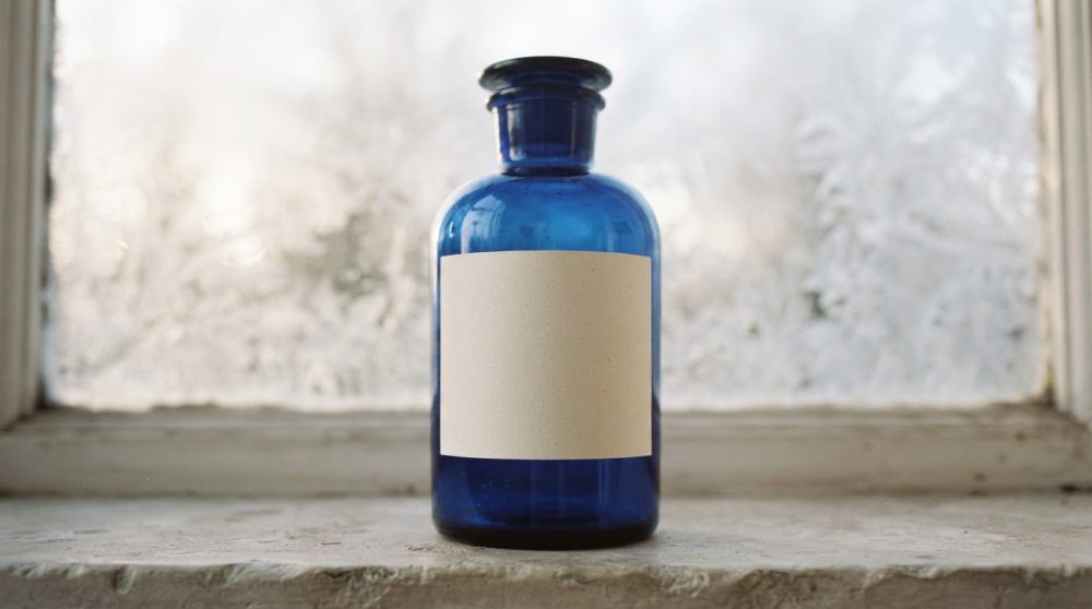Frasco azul vintage com rótulo branco vazio numa janela com vidro fosco