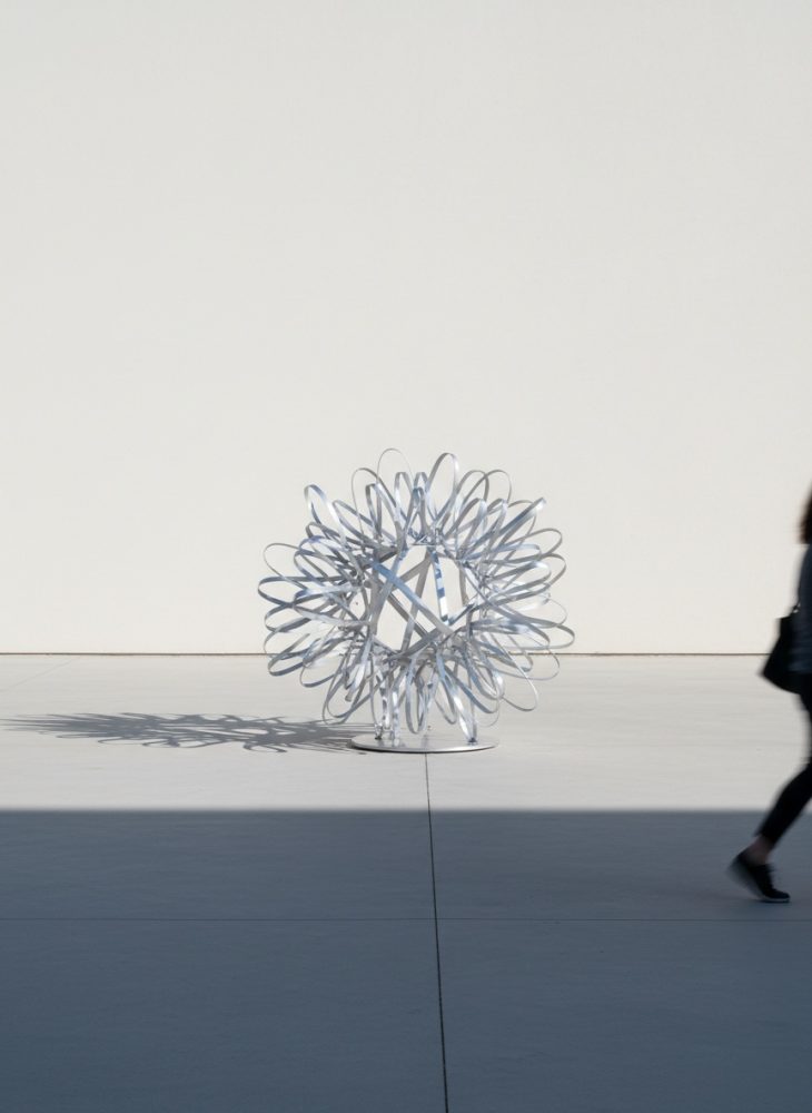 Escultura abstracta metálica circular com sombra definida numa superfície clara