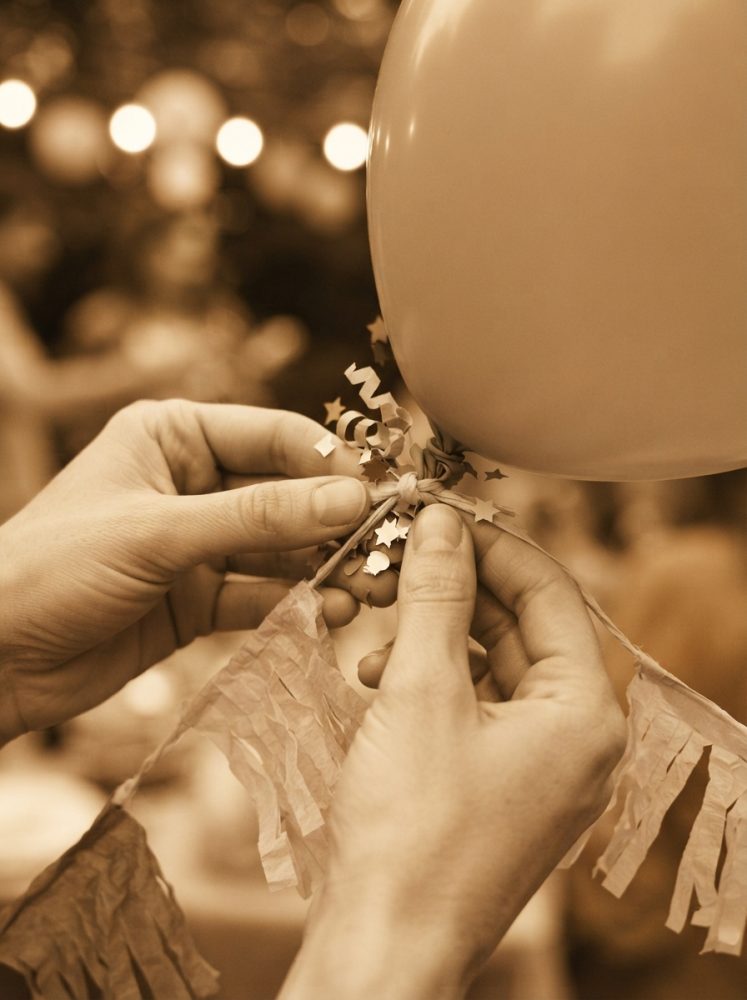 Mãos a atar fitas decorativas com estrelas a um balão para festa