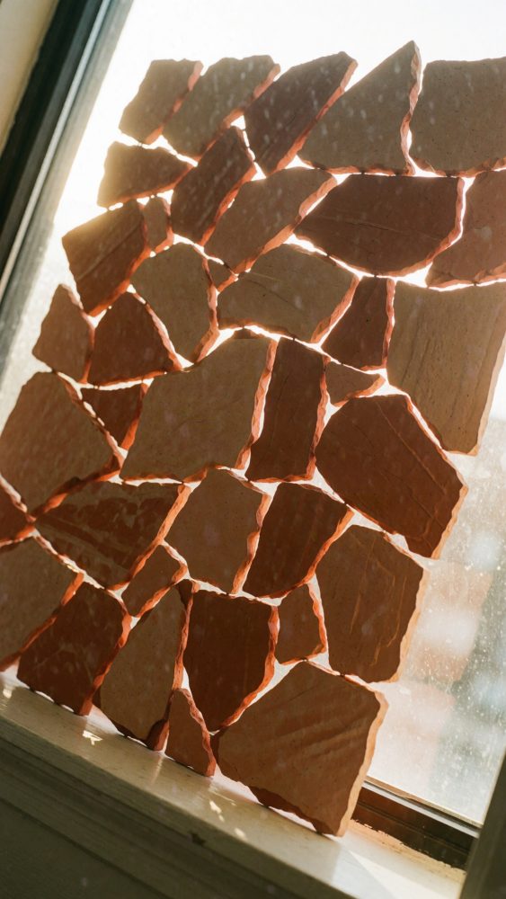 Painel de azulejos terracota quebrados iluminado pela luz natural numa janela